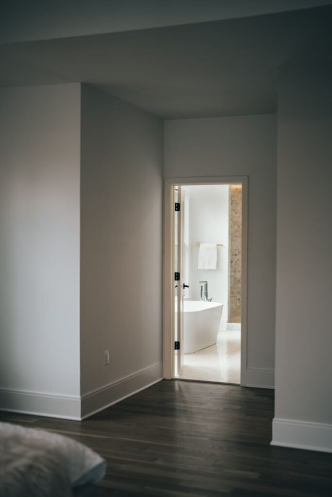 A glimpse into a modern bathroom with a sleek bathtub, seen through an open doorway.